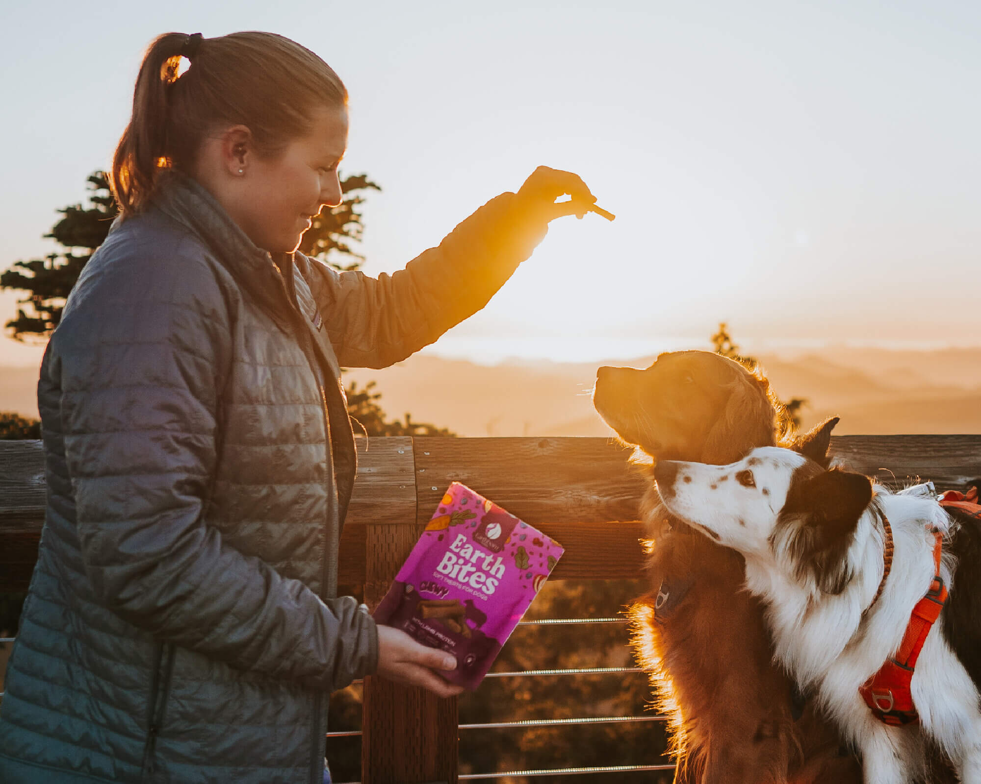 Woman rewarding two dogs with EarthBites Chewy lamb protein treats at sunset