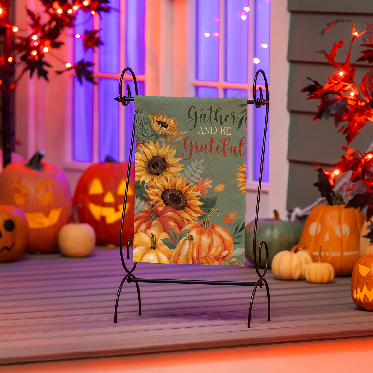 Evergreen Grateful Gatherings Suede Garden Flag -- displayed on a porch with jack-o-lanterns at dusk
