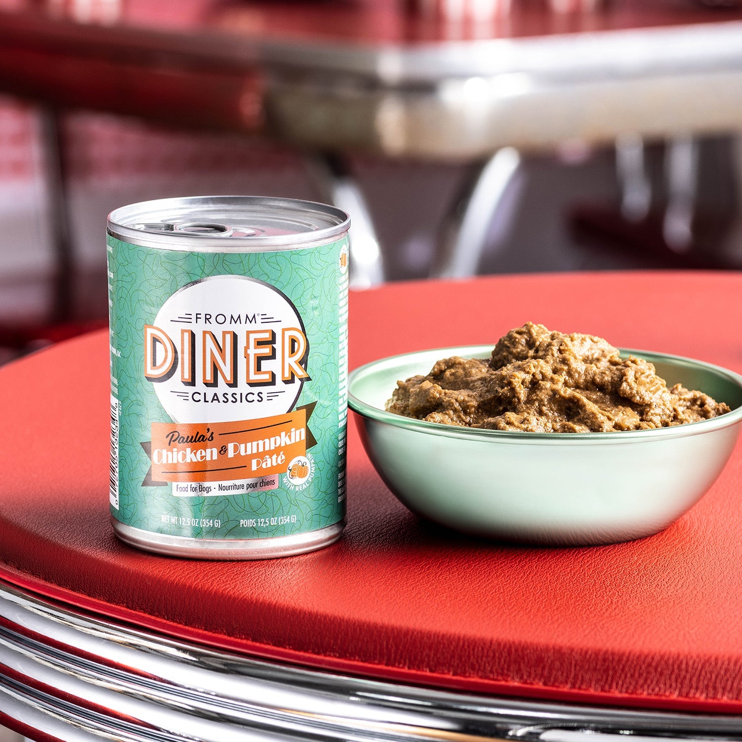 A can of Fromm Diner Classics Paula's Chicken & Pumpkin Pâté beside a bowl of pâté on a red retro diner table