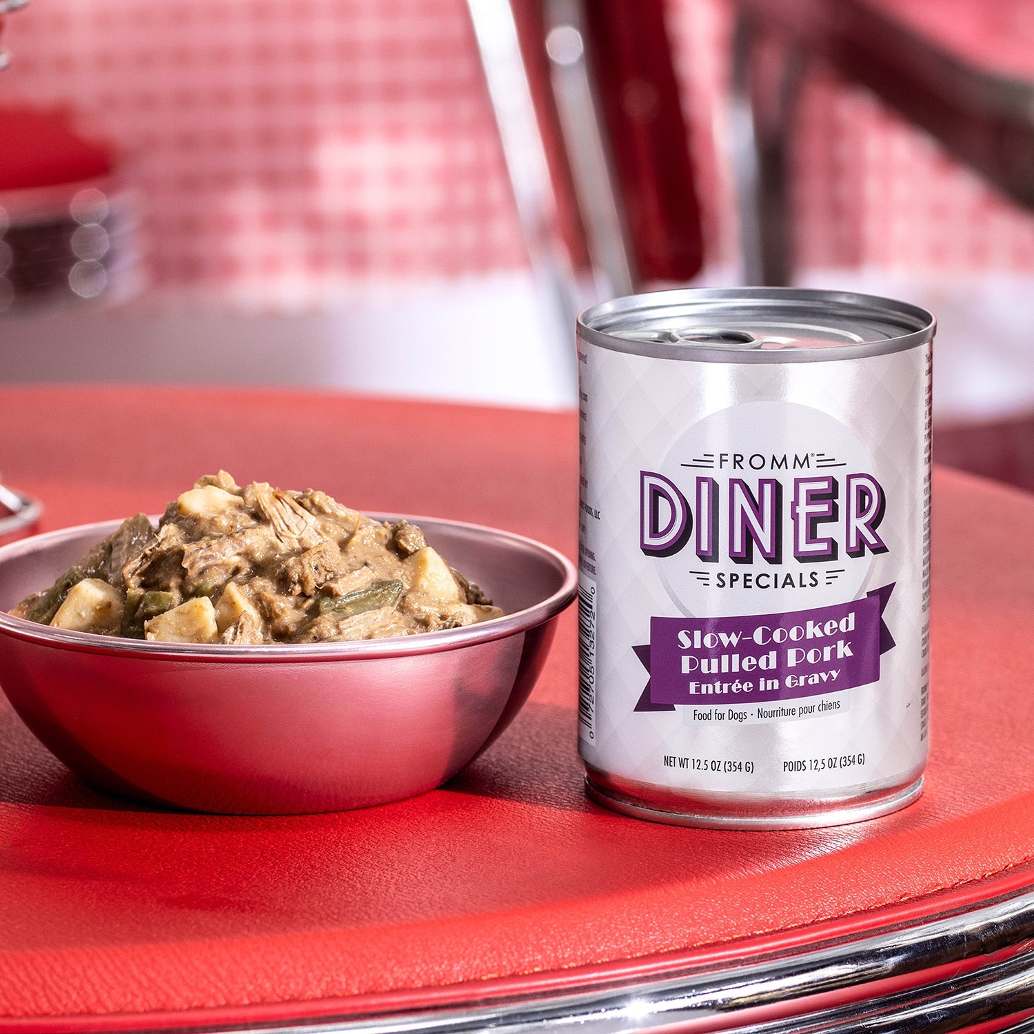 A can of Fromm Diner Specials Slow-Cooked Pulled Pork beside a bowl of pulled pork entrée on a retro diner table