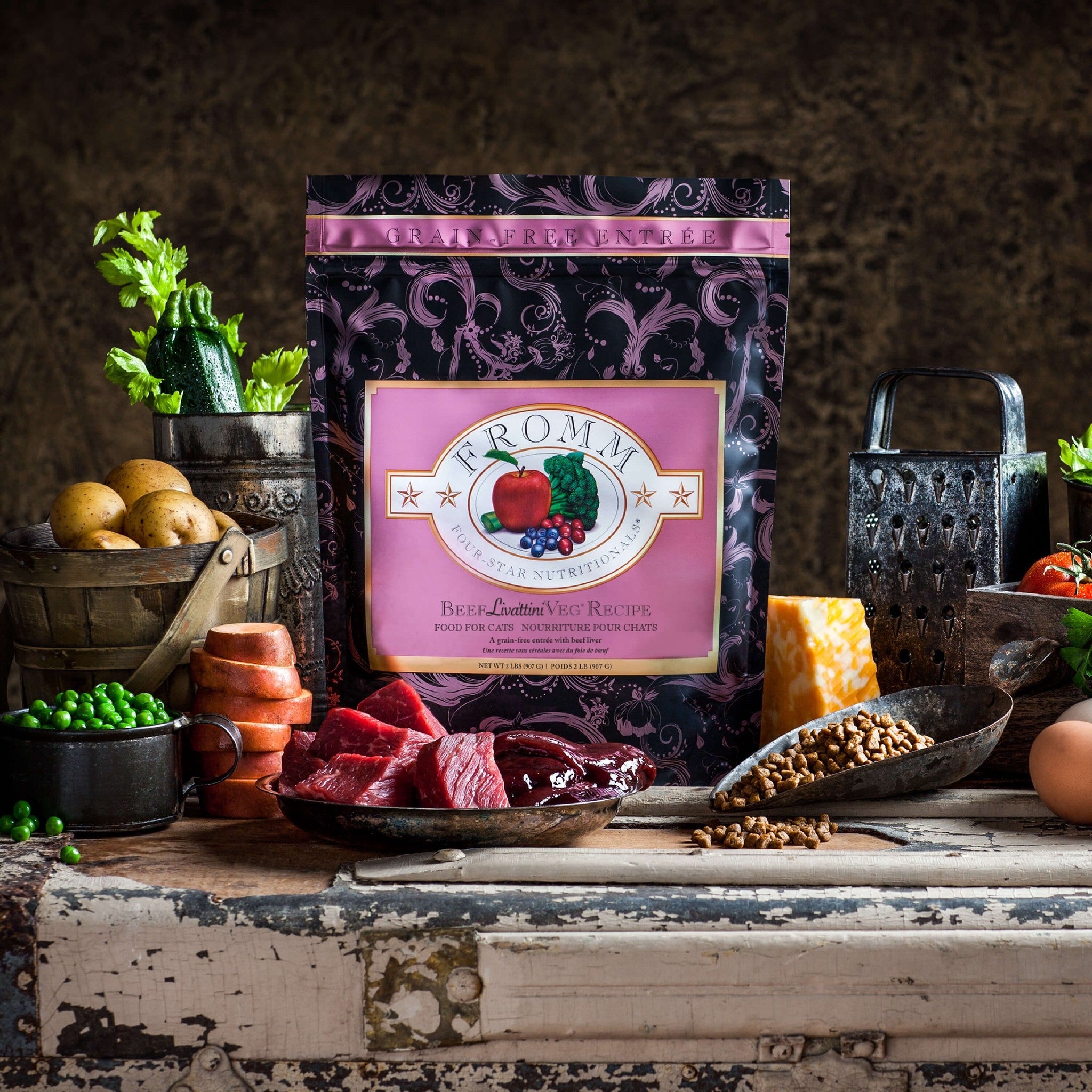 A bag of Fromm Four-Star Beef Liváttini Veg surrounded by raw beef, liver, peas, potatoes, and cheese with a scoop of kibble