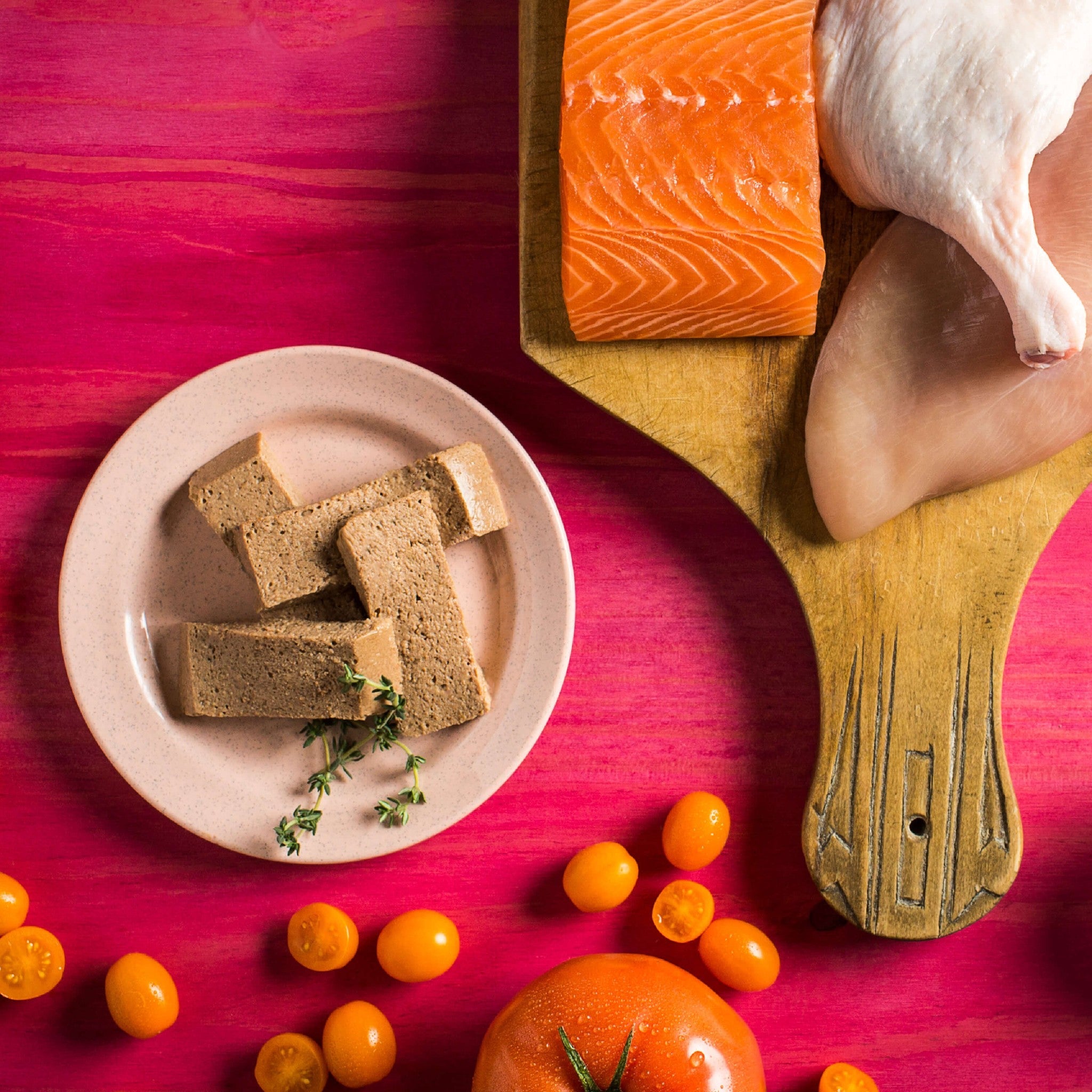 Raw ingredients for Fromm Four-Star Chicken, Duck & Salmon Pâté: salmon fillet, whole chicken, tomatoes, and sliced pâté on a plate