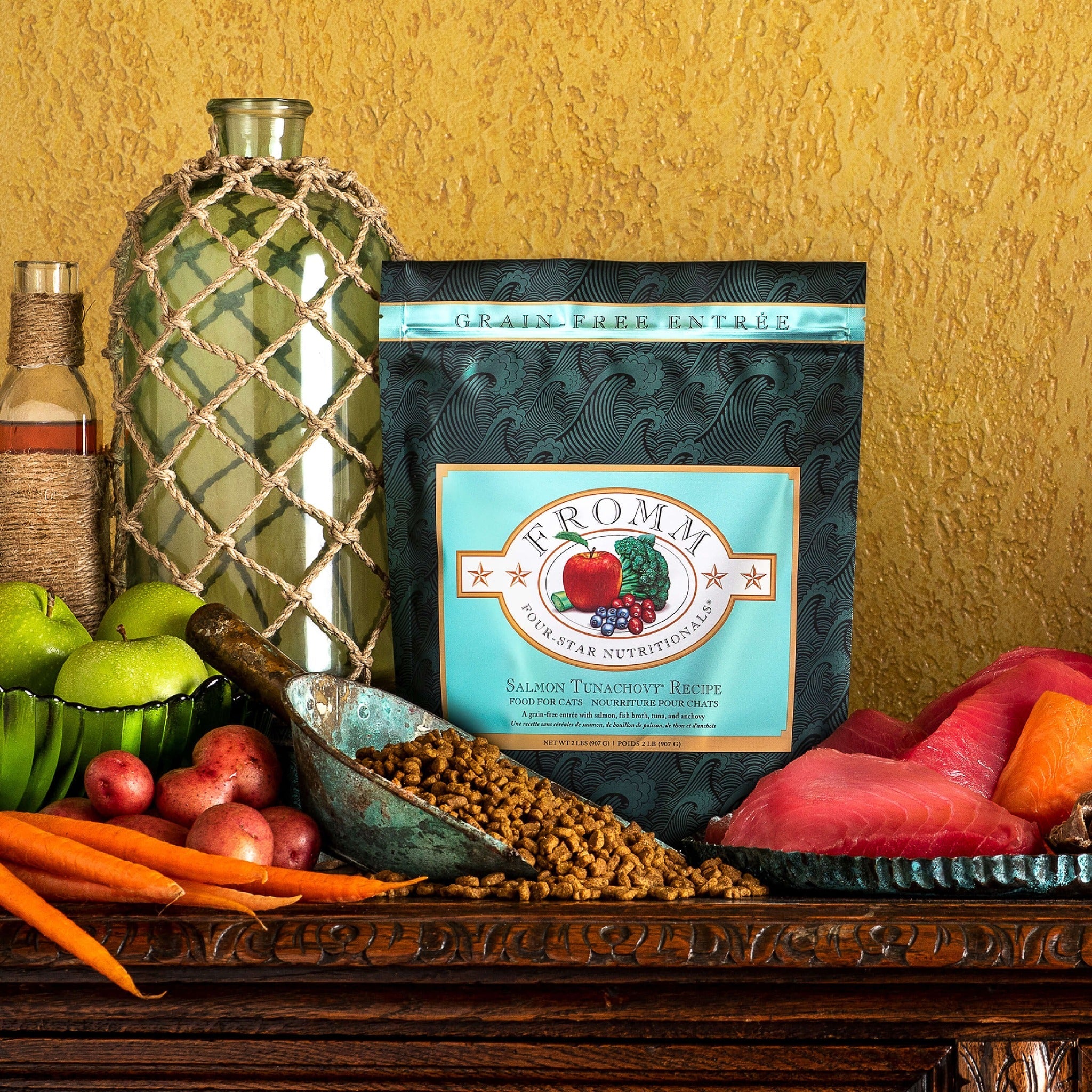 Fromm Four-Star Salmon Tunachovy Recipe Cat Food bag styled with fresh salmon and tuna fillets, apples, potatoes, and carrots
