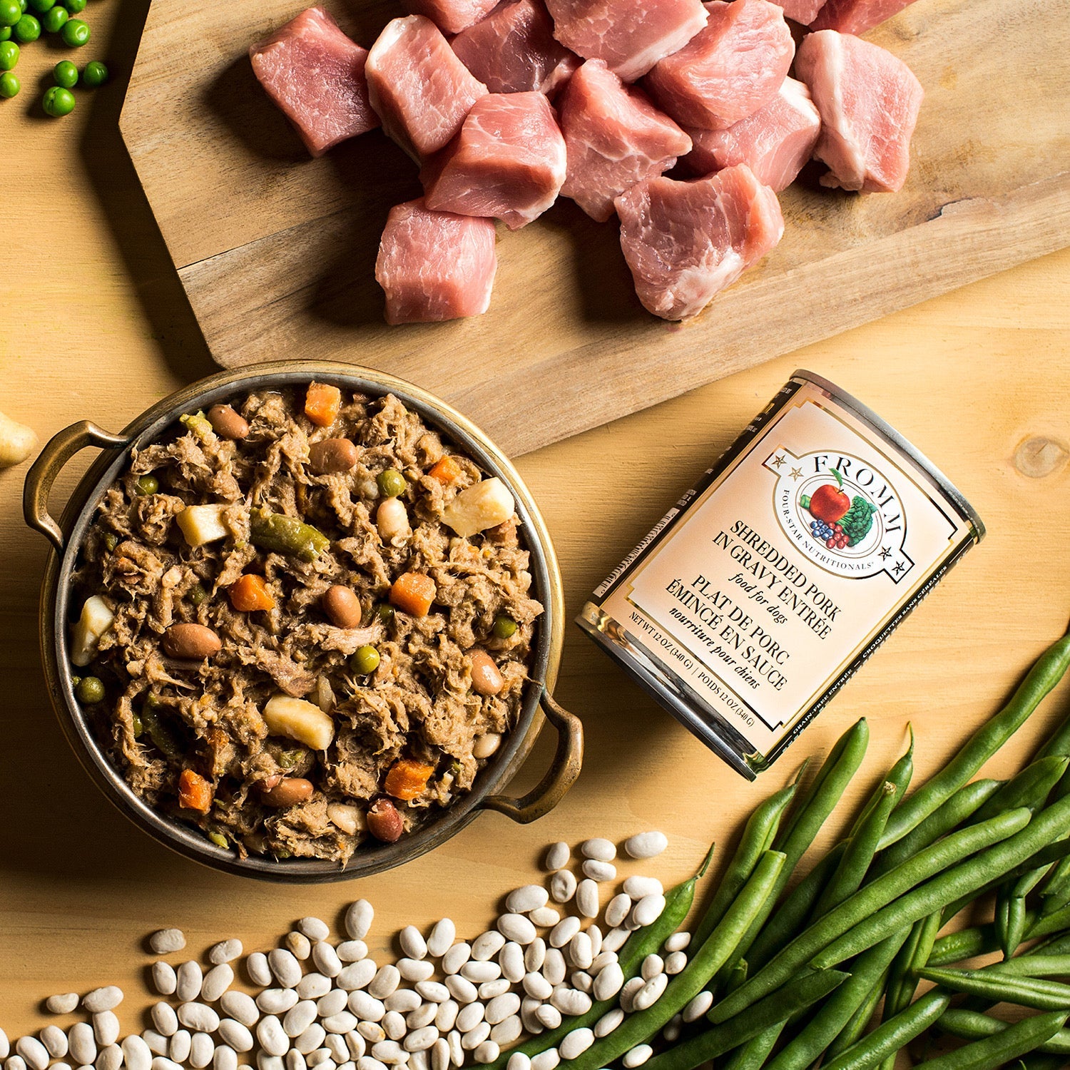 A can of Fromm Shredded Pork in Gravy Entrée beside a bowl of shredded pork food with raw pork, green beans, white beans, and peas