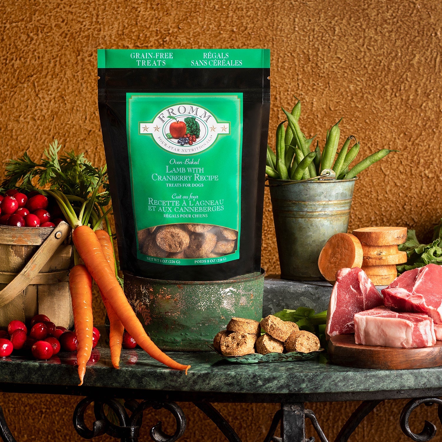 Fromm Four-Star Lamb with Cranberry treats bag styled with raw lamb chops, carrots, cranberries, sweet potatoes, and green beans