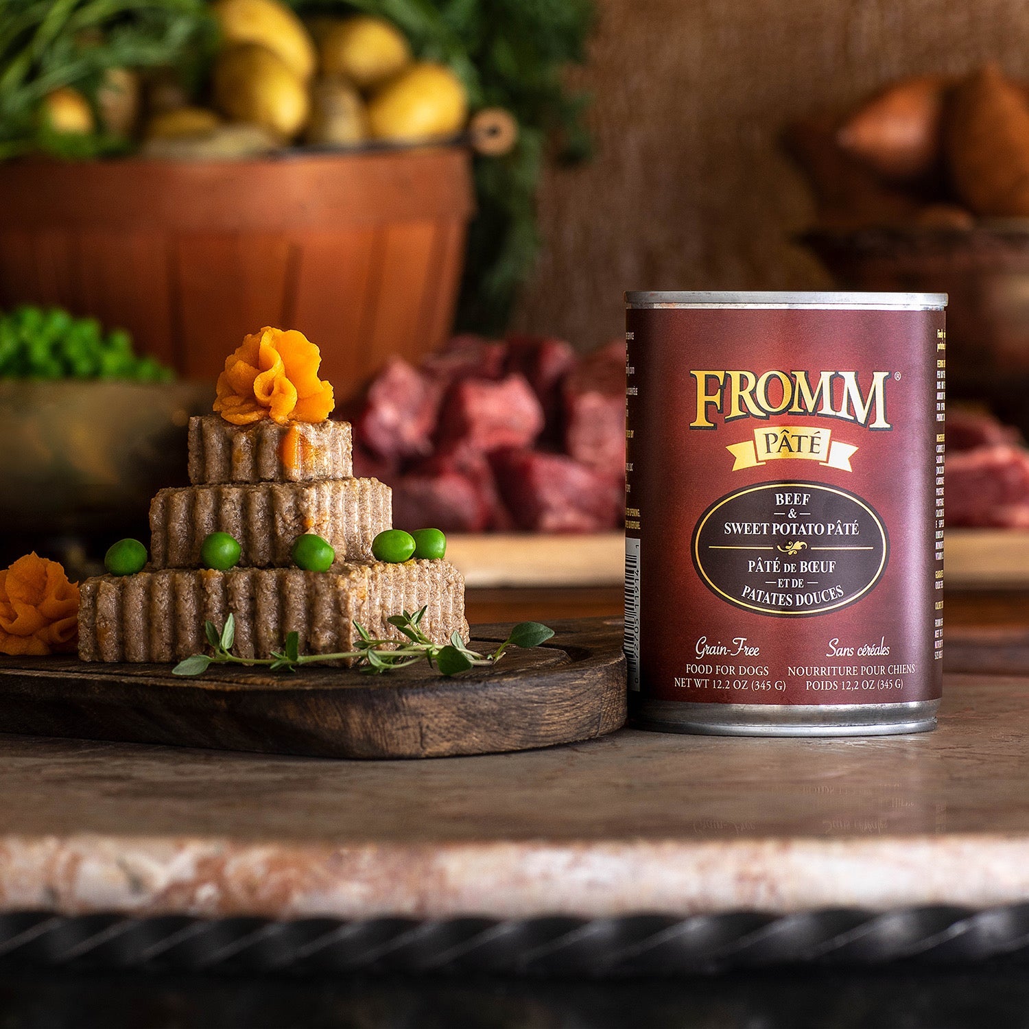 A can of Fromm Pâté Beef & Sweet Potato beside a stacked pâté garnished with sweet potato and peas on a wooden board