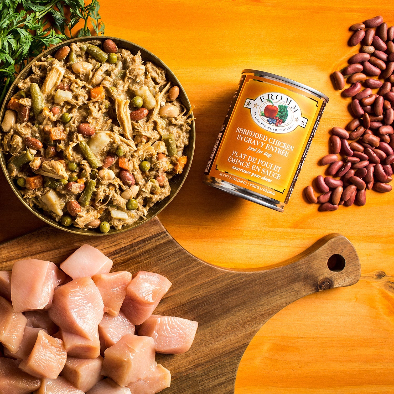 A can of Fromm Four-Star Shredded Chicken in Gravy Entrée beside an opened can of shredded chicken food with raw chicken, kidney beans, and carrot greens