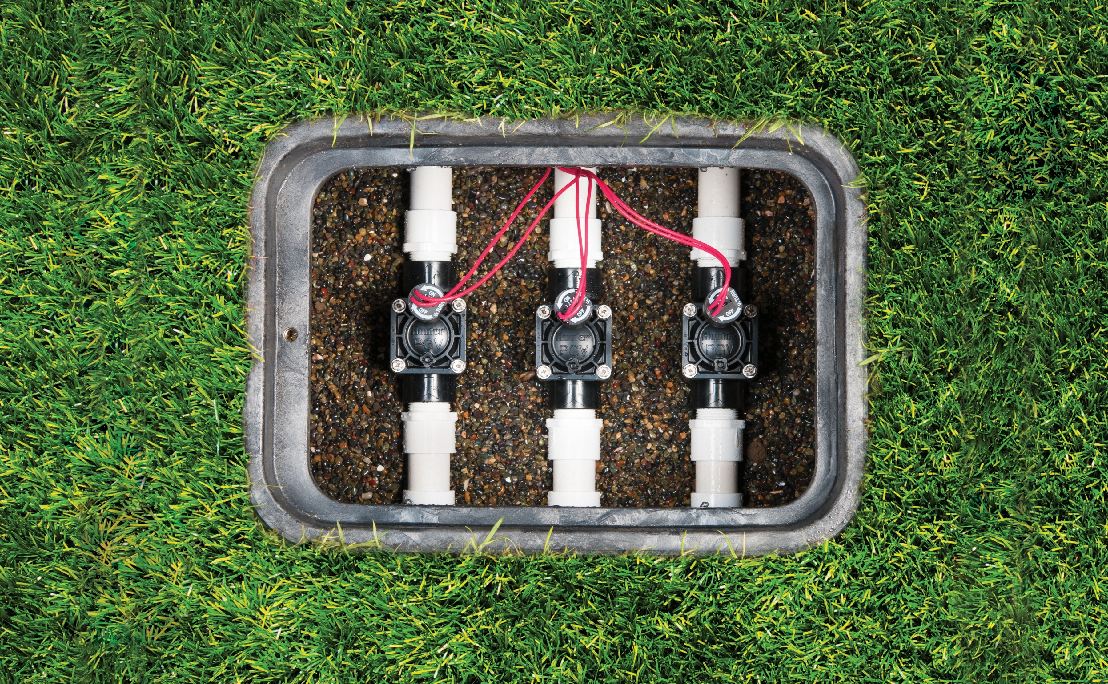 Three Hunter PGV-100 1 in. irrigation valves installed in a manifold inside an in-ground valve box on a residential lawn