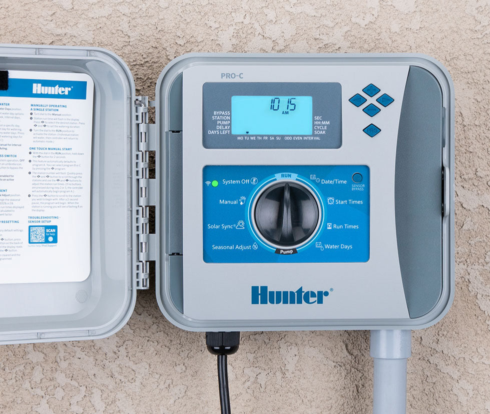 Hunter P2C-400 Pro-C controller mounted on an exterior stucco wall with door open showing the programming sticker and face panel