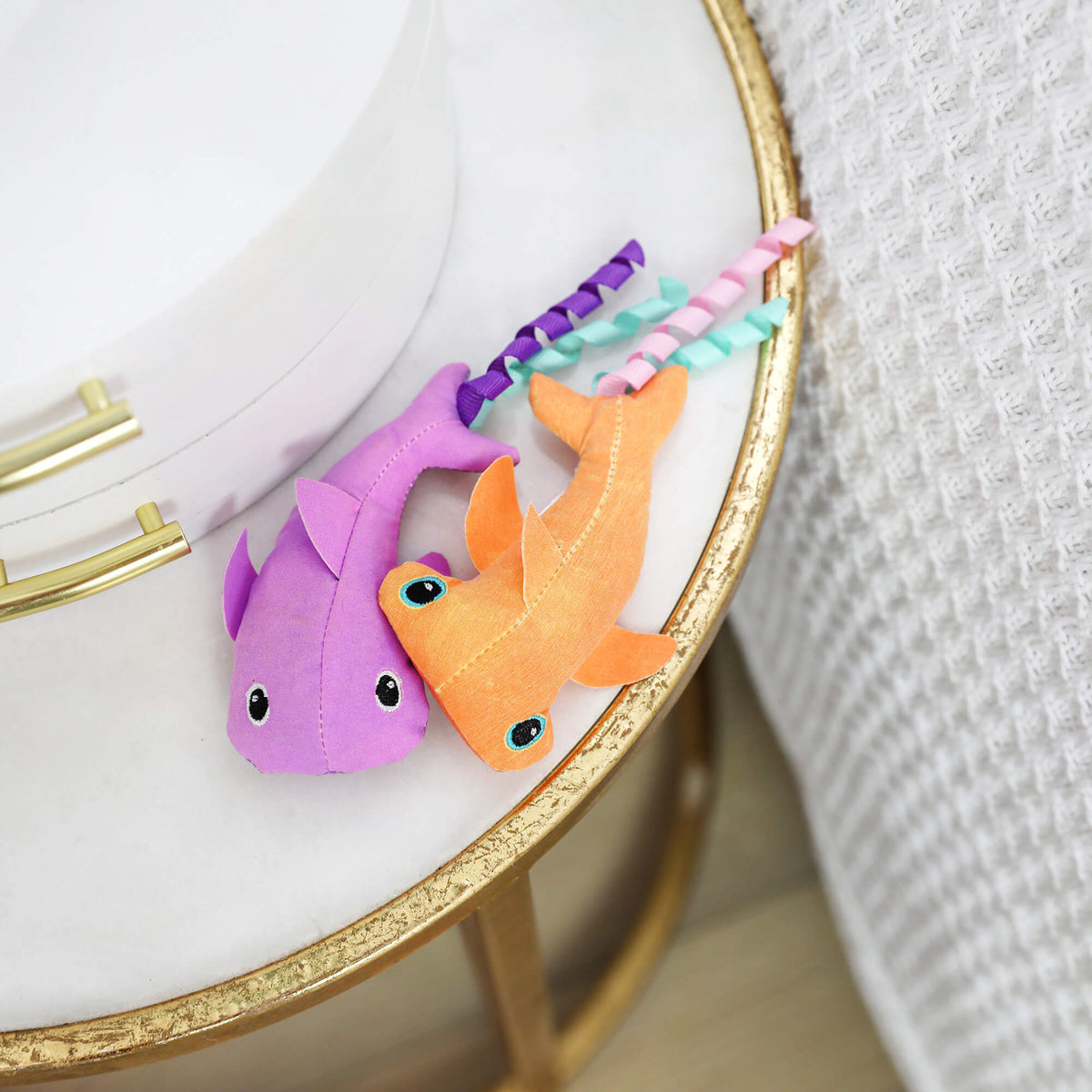 Purple and orange Cool Sharks cat toys with curly ribbons on a marble and gold side table