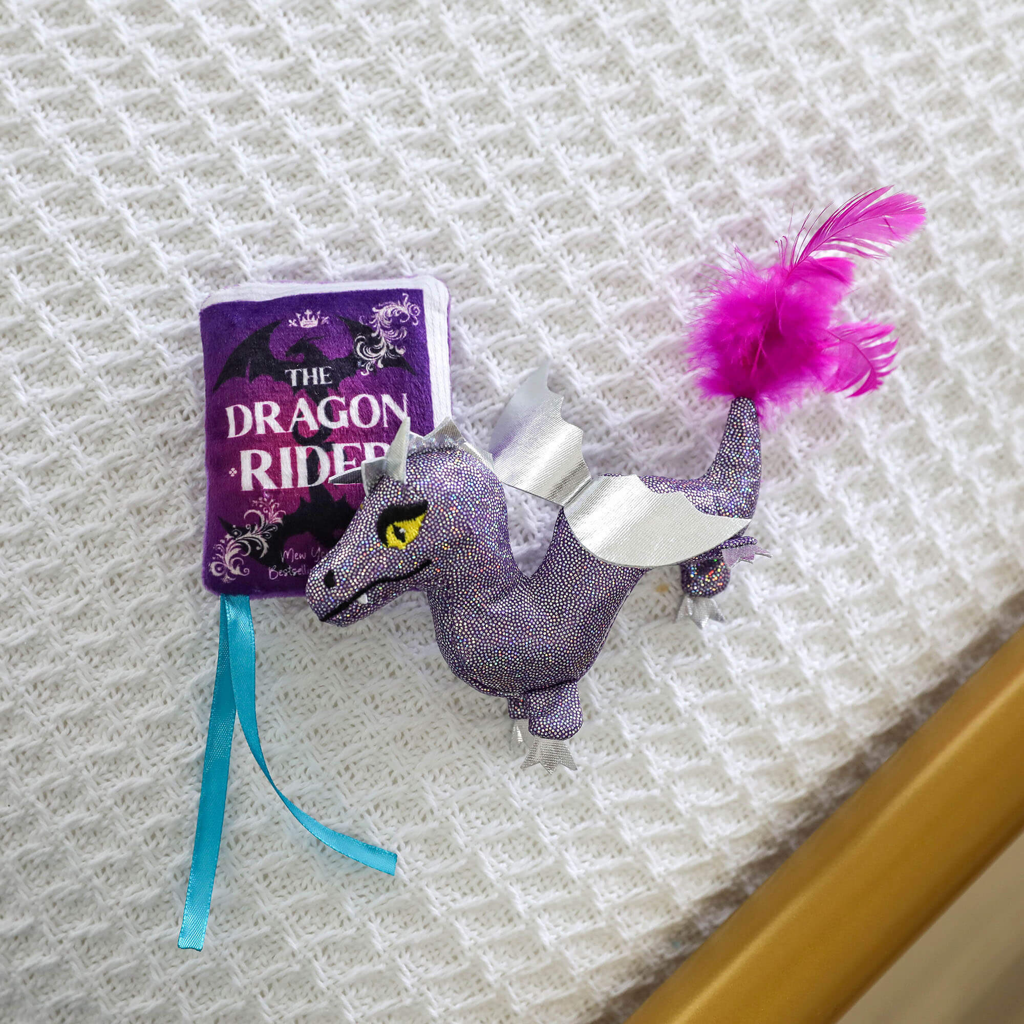 Plush Dragon Rider storybook and glittery purple dragon cat toys laid on a white knit blanket