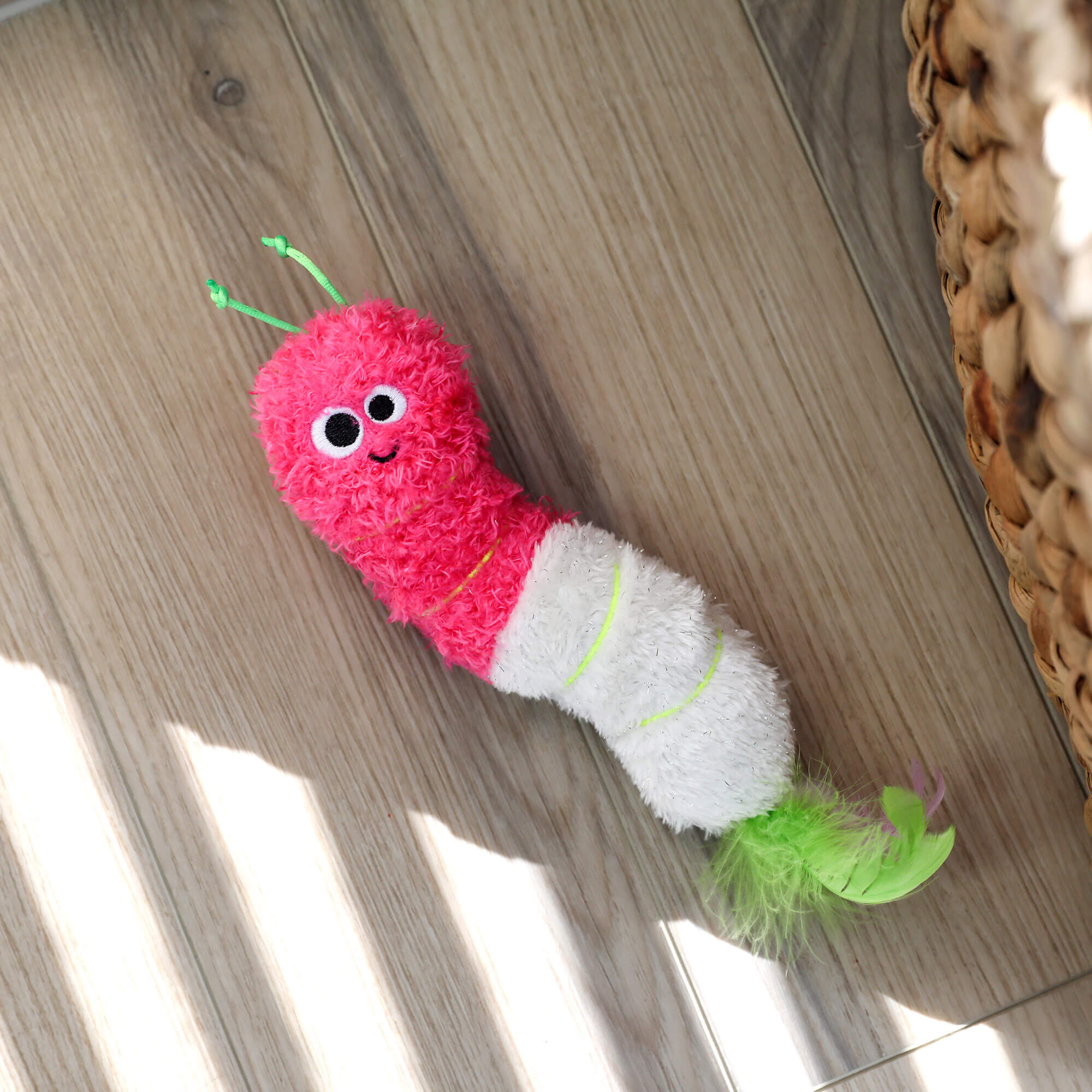 Quirky Kitty Glow Worm Kicker lying on a wood floor beside a woven basket