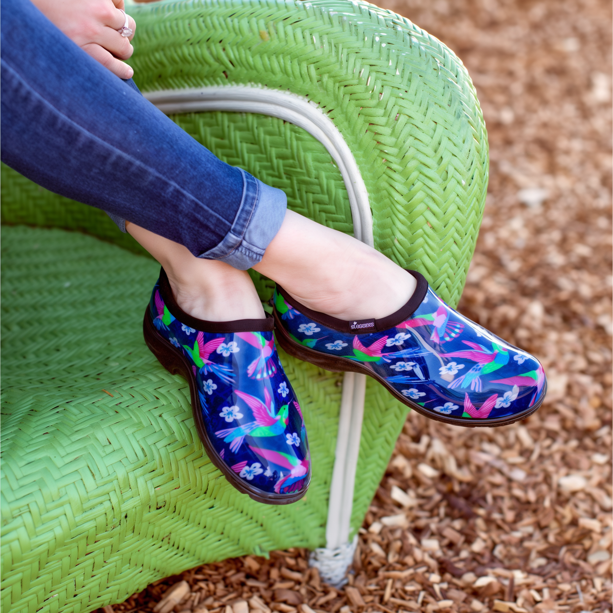 Sloggers Hummingbird Blue-Pink garden shoes alongside a watering can and garden tools