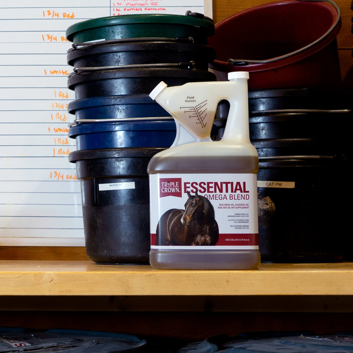 Triple Crown Essential Omega Blend jug on a feed room shelf beside stacked buckets