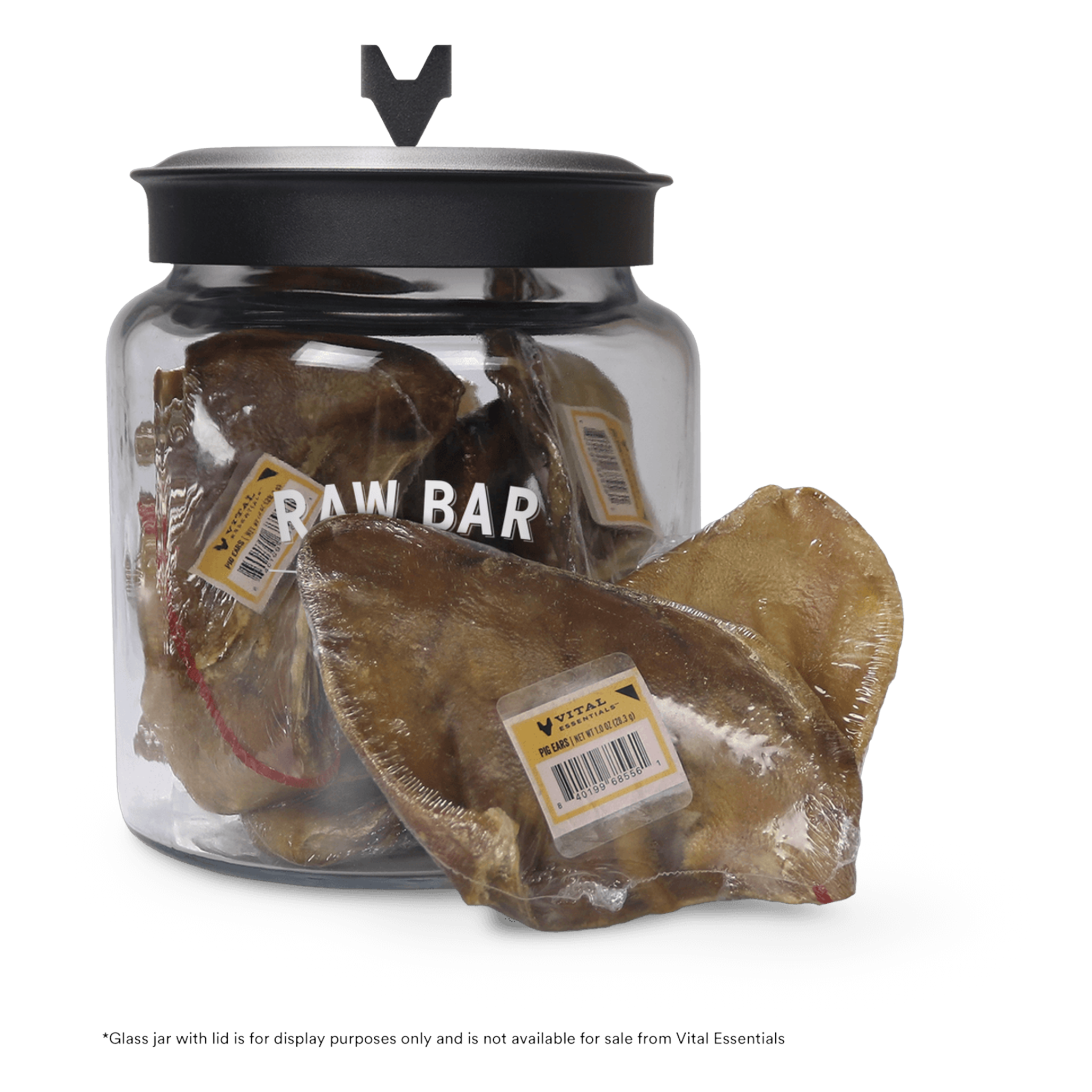 Vital Essentials Raw Bar shrink-wrapped single pig ear dog chew with band label in front of the Raw Bar display jar