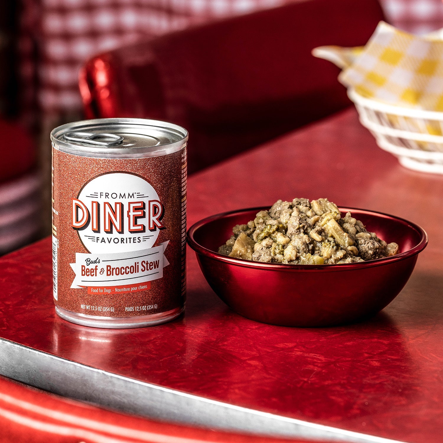 A can of Fromm Diner Favorites Bud's Beef & Broccoli Stew beside a red bowl of the stew on a retro diner table