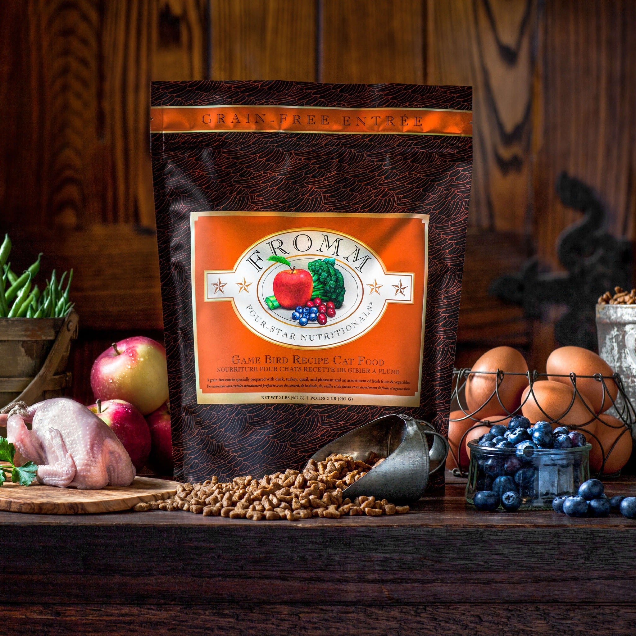 Fromm Four-Star Game Bird bag surrounded by fresh green beans, apples, brown eggs, blueberries, a dressed game bird, and a scoop of kibble