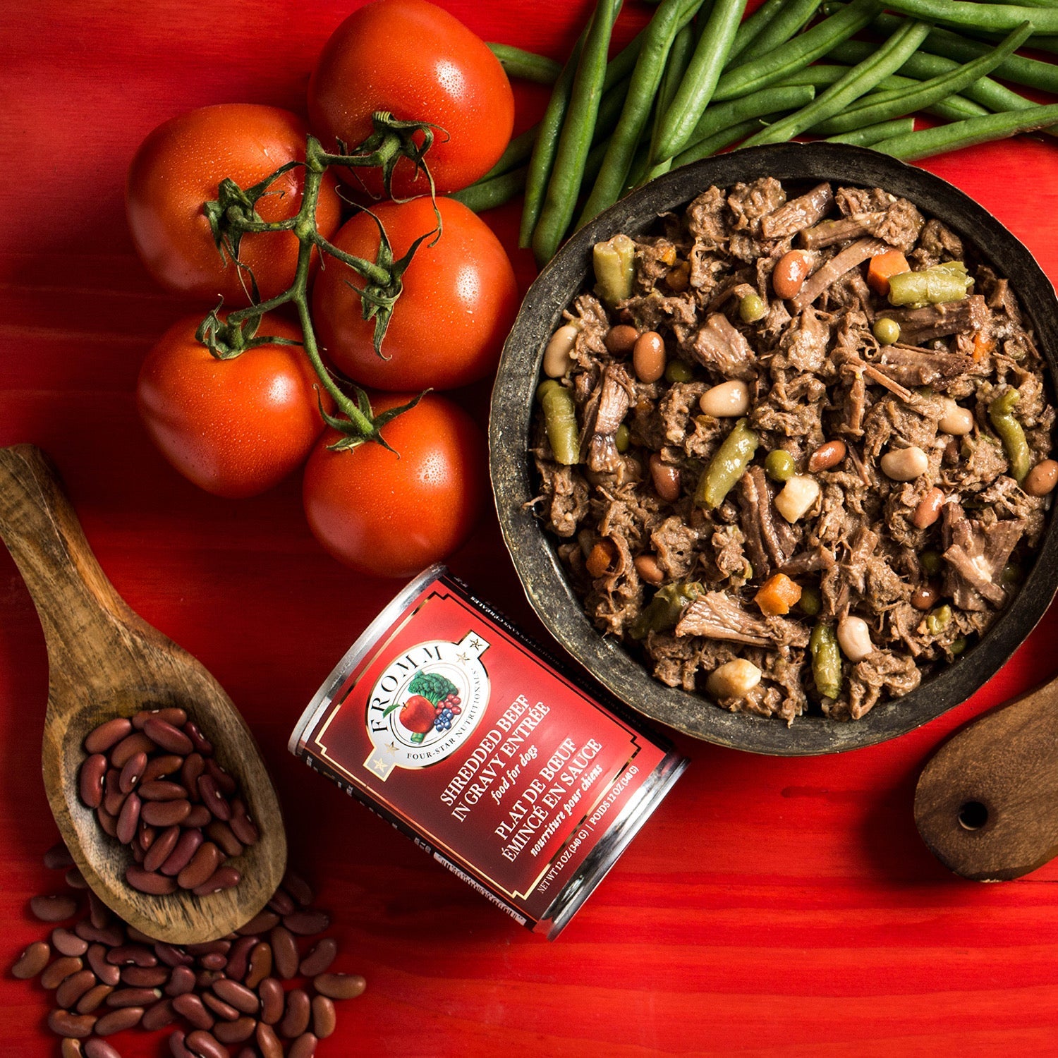 A bowl of Fromm Four-Star Shredded Beef in Gravy Entrée beside the can with vine tomatoes, green beans, and kidney beans