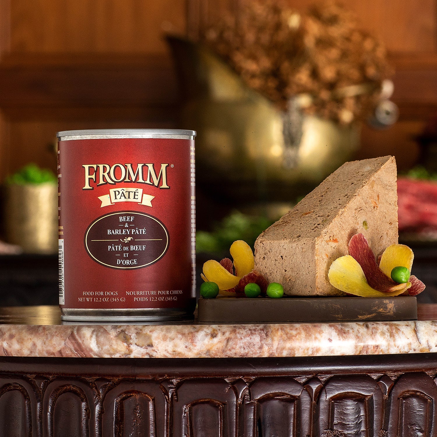 A can of Fromm Pâté Beef & Barley beside a sliced pâté garnished with peas and carved carrots on a marble table