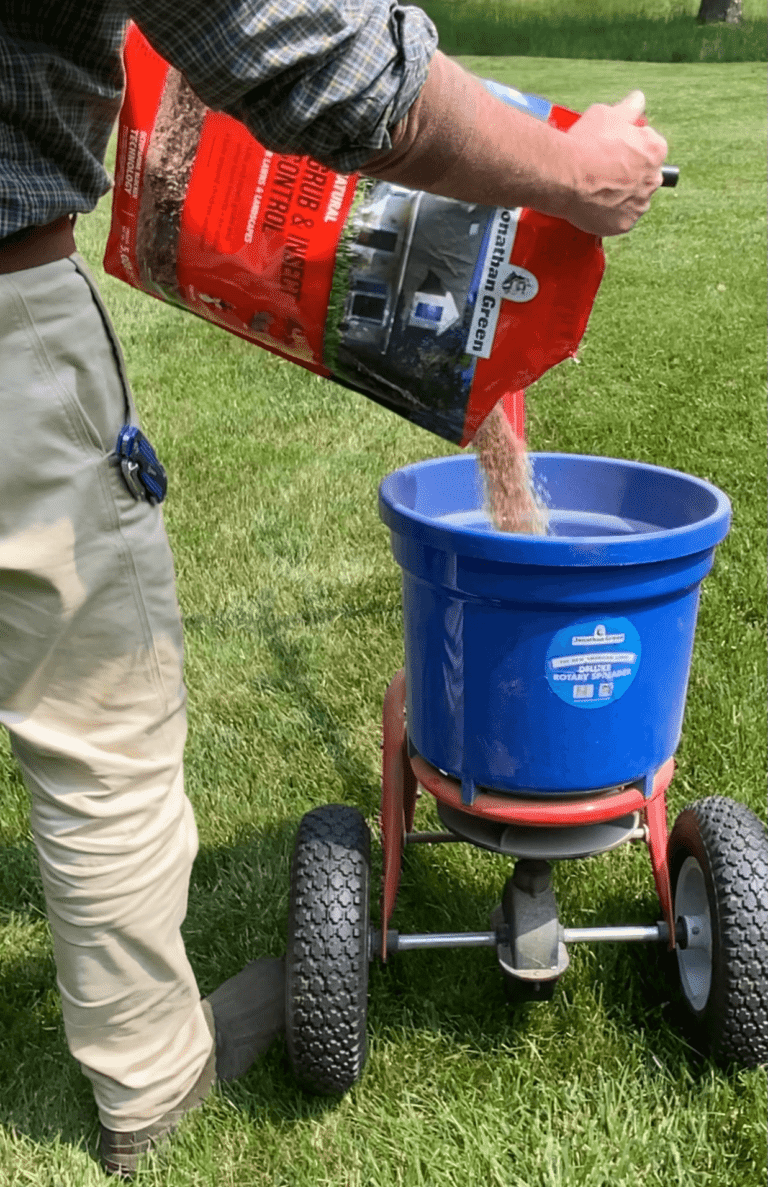 Lifestyle photo of Jonathan Green Natural Grub & Insect Control granules being poured from the bag into a broadcast spreader hopper for application to a residential lawn