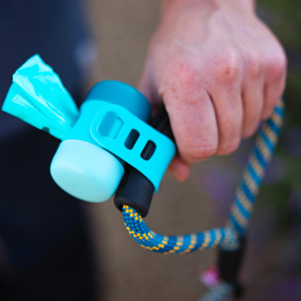 Hand holding a leash with the Messy Mutts dispenser strapped on and a bag pulled out