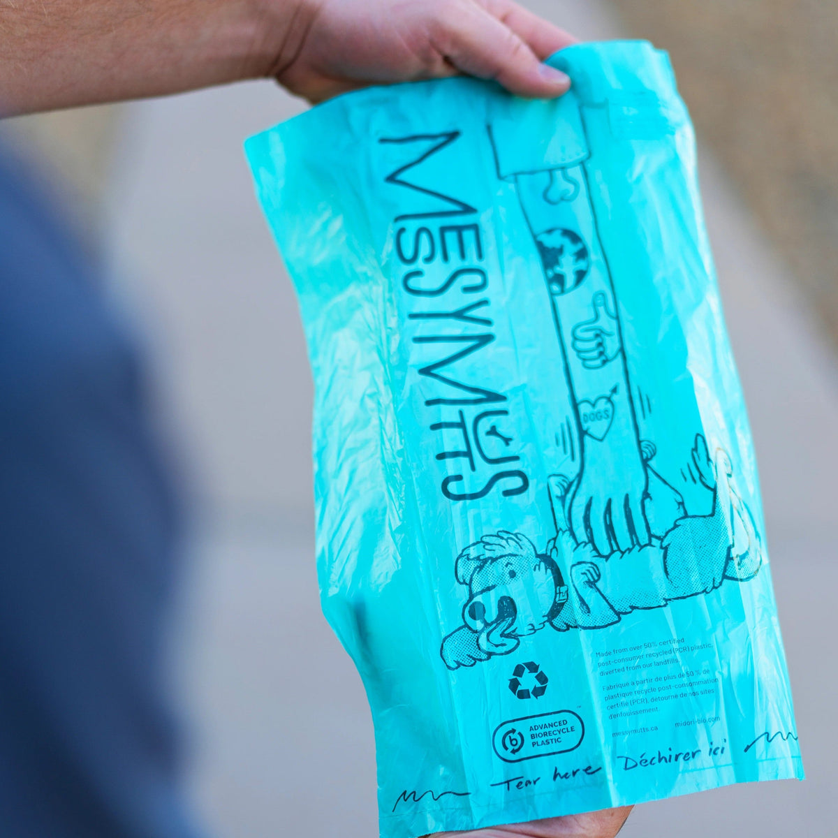 Teal Messy Mutts poop bag held open outdoors
