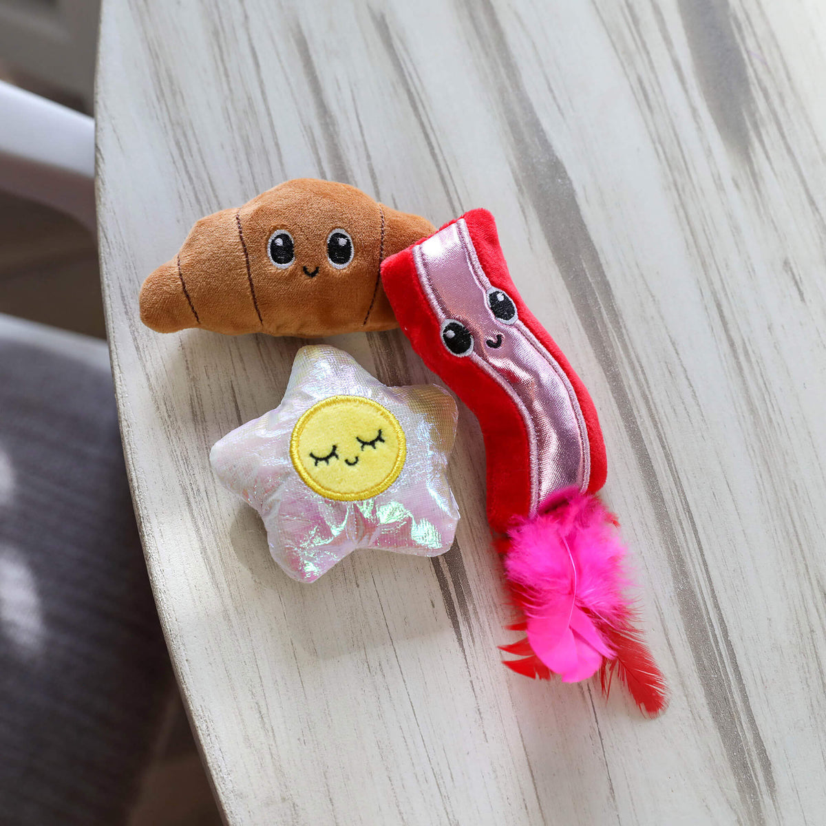 Brunch Bunch plush croissant, iridescent fried egg and feathered bacon toys on a whitewashed table