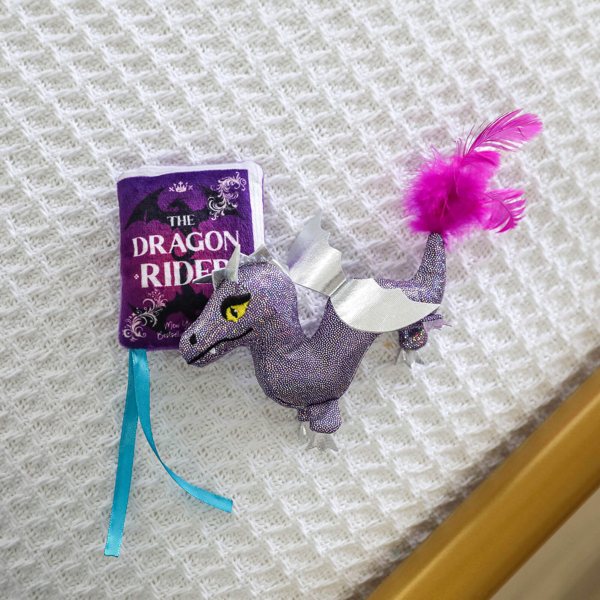 Plush Dragon Rider storybook and glittery purple dragon cat toys laid on a white knit blanket