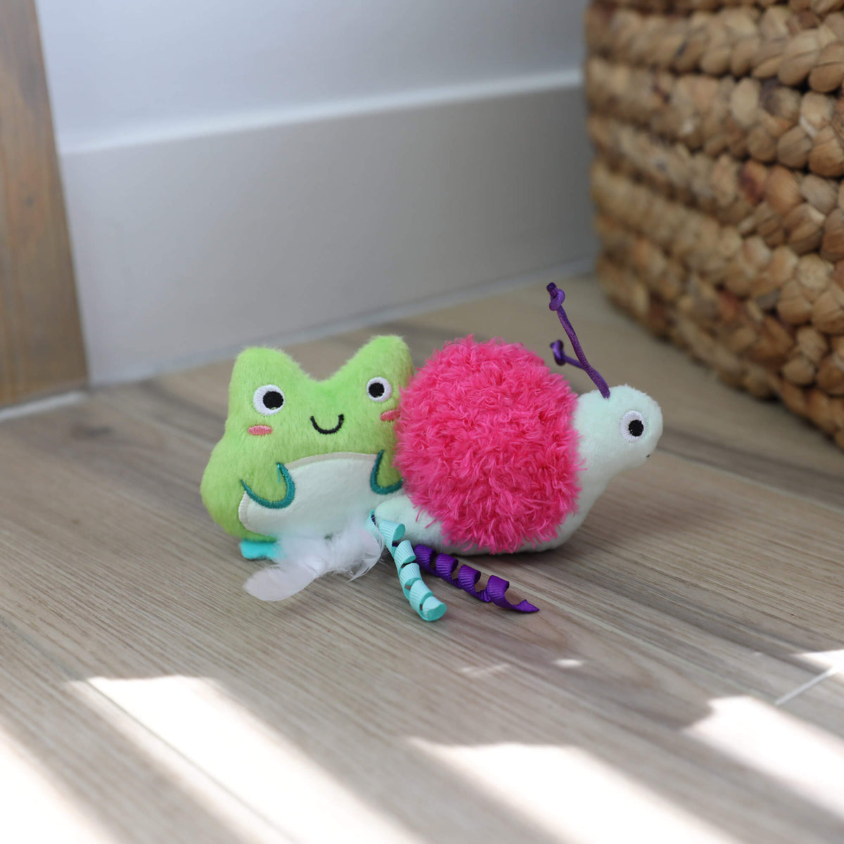 Quirky Kitty Glow Critters frog and snail toys on a wood floor beside a woven basket