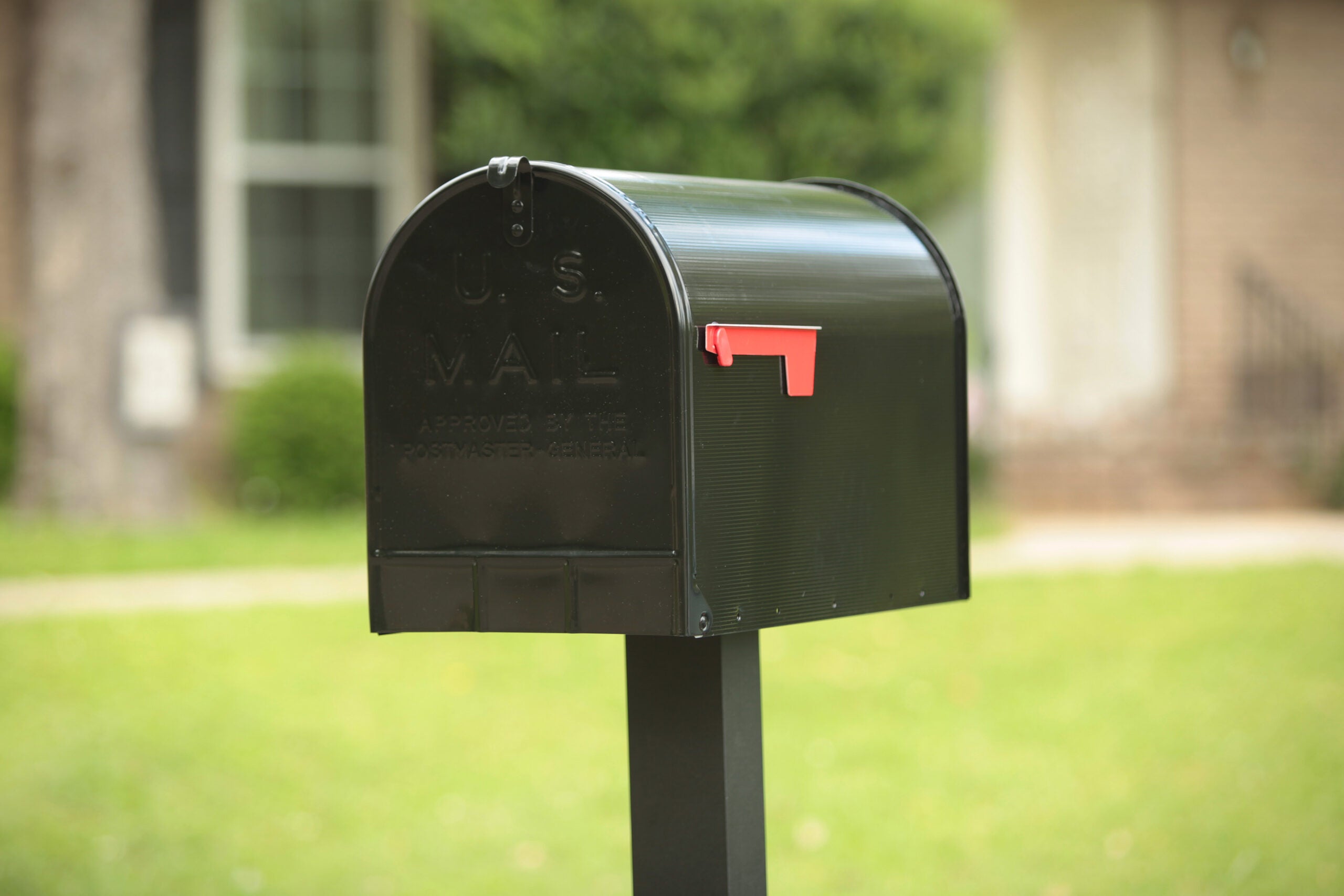 Black Stanley mailbox with red flag raised on a post in a sunny front yard