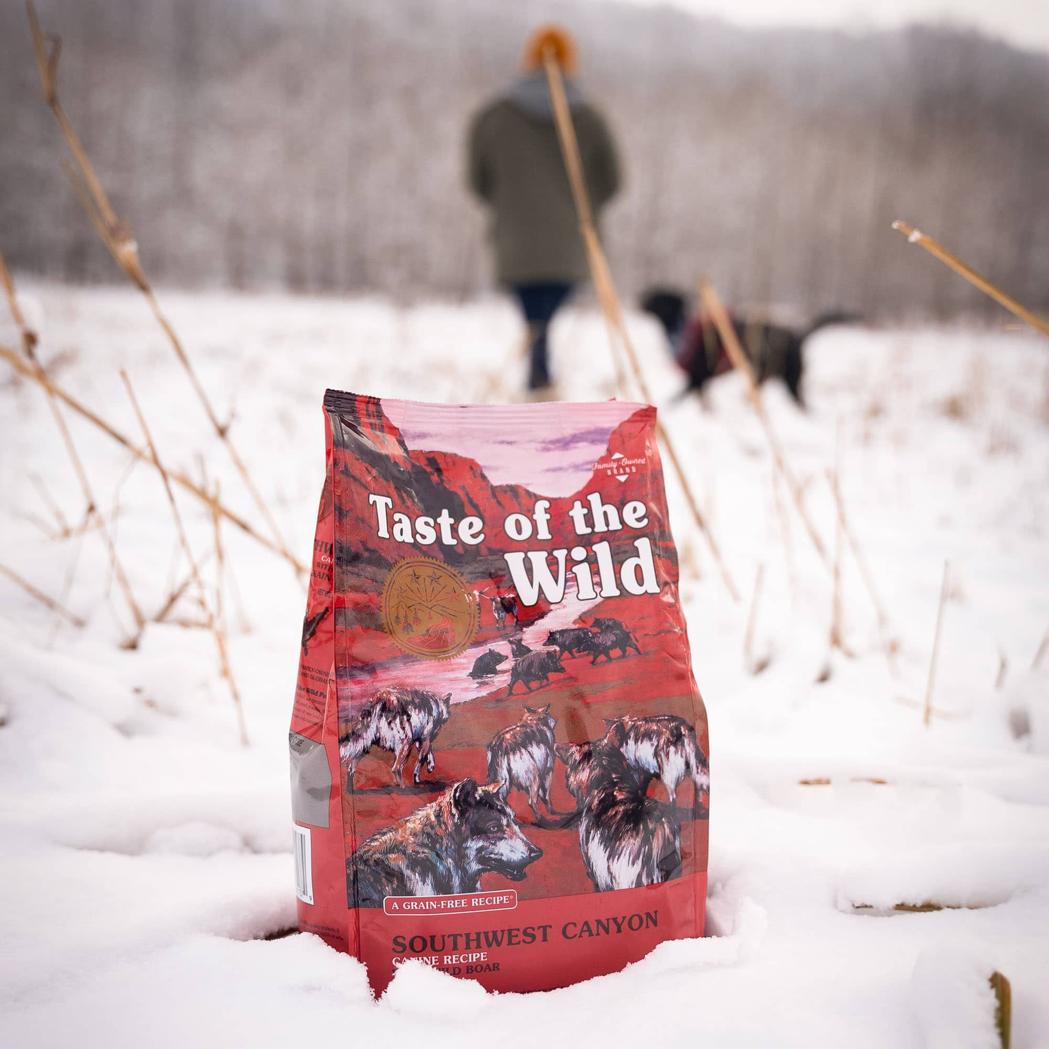Bag of Taste of the Wild Southwest Canyon standing in the snow while a walker and dog pass in the background
