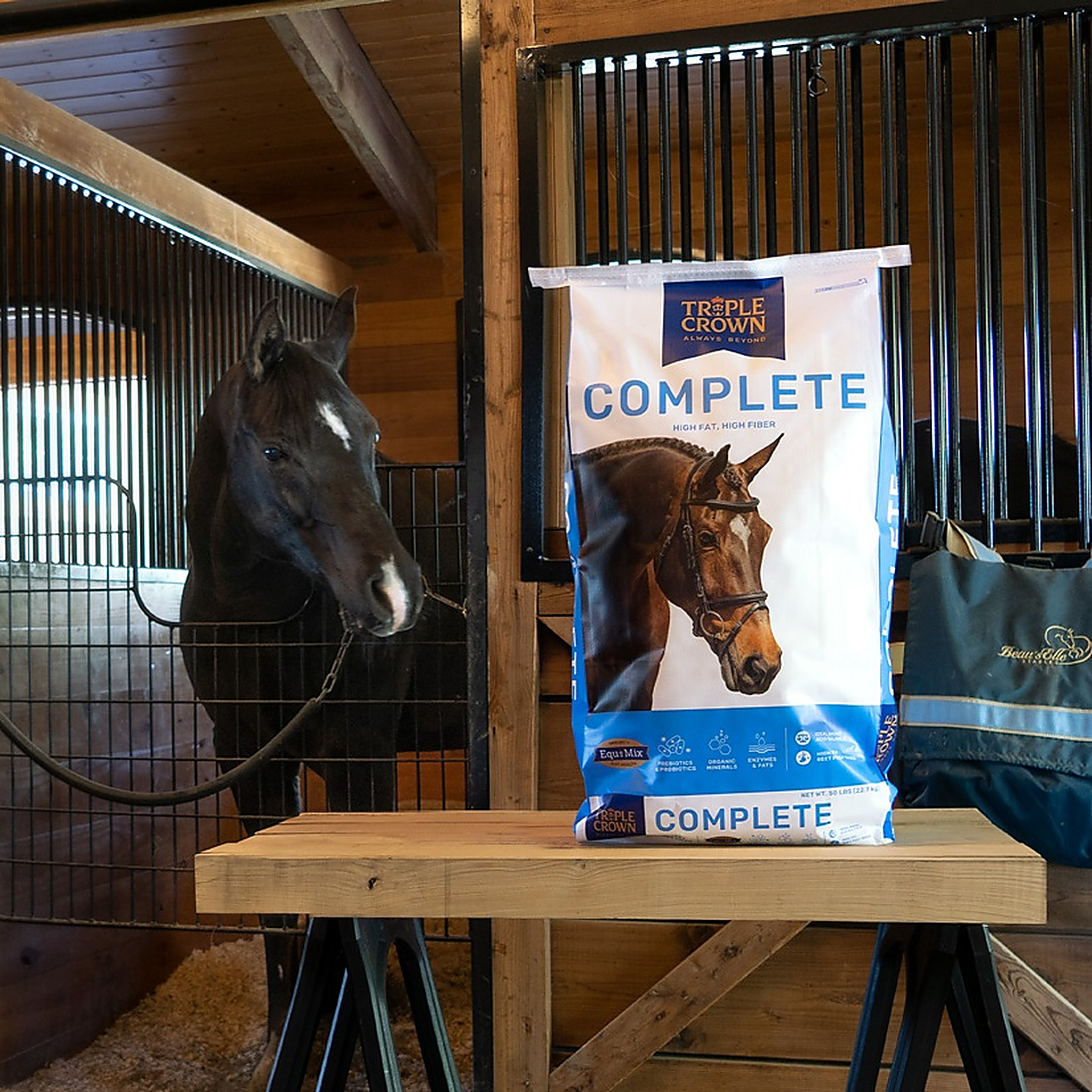 Triple Crown Complete 50 lb bag on a barn table with a dark bay horse looking on