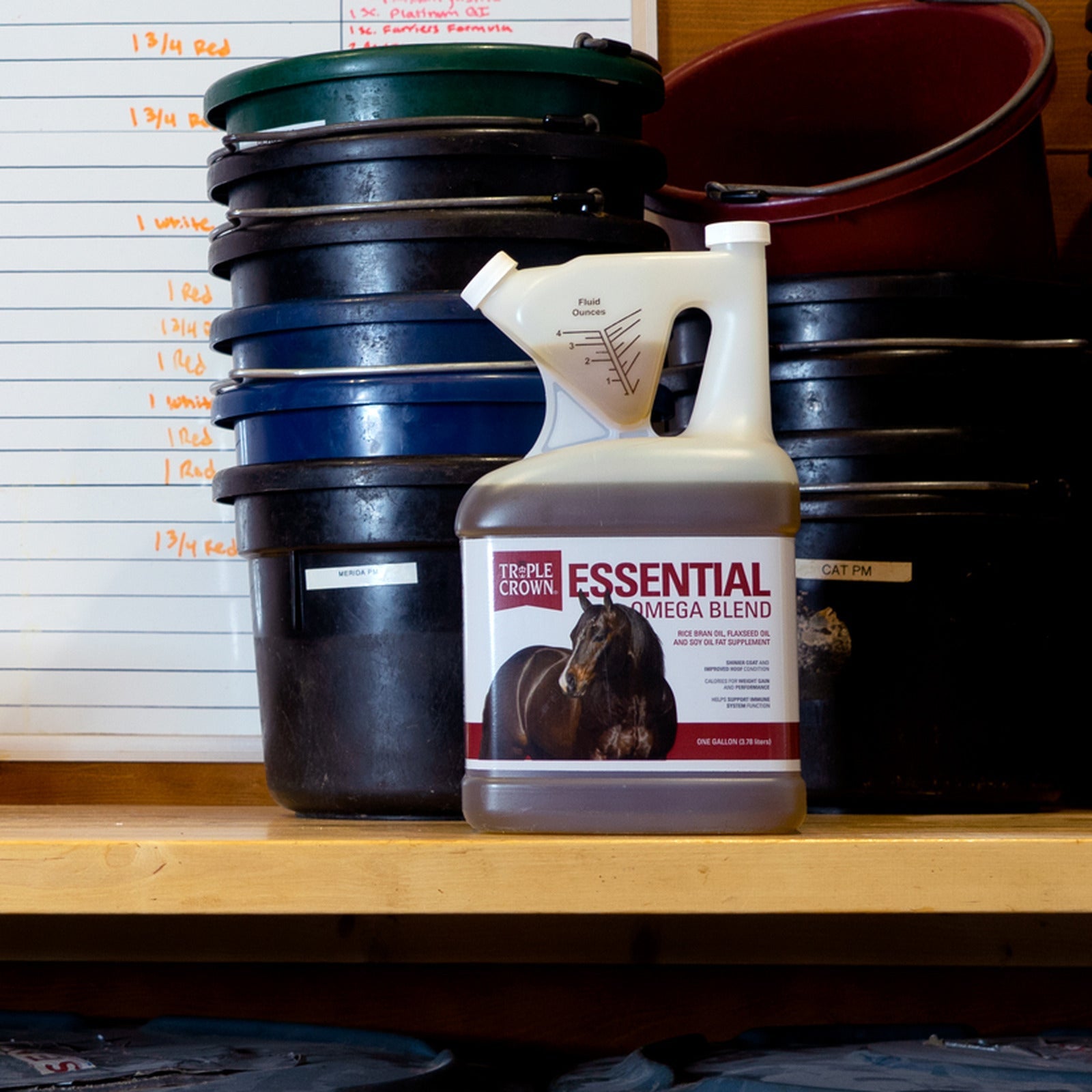 Triple Crown Essential Omega Blend jug on a feed room shelf beside stacked buckets