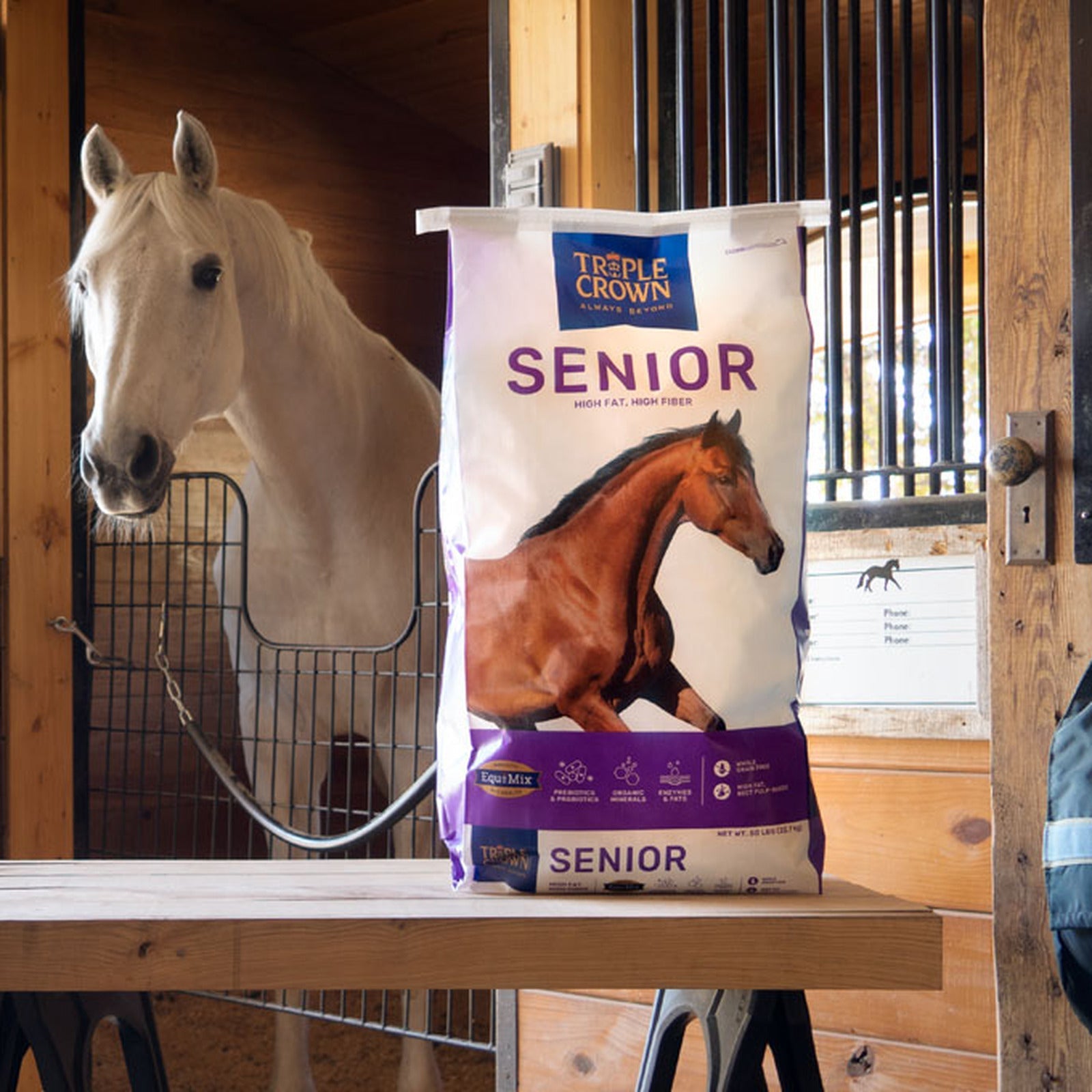 Triple Crown Senior bag on a feed stand in a barn aisle beside a horse in its stall