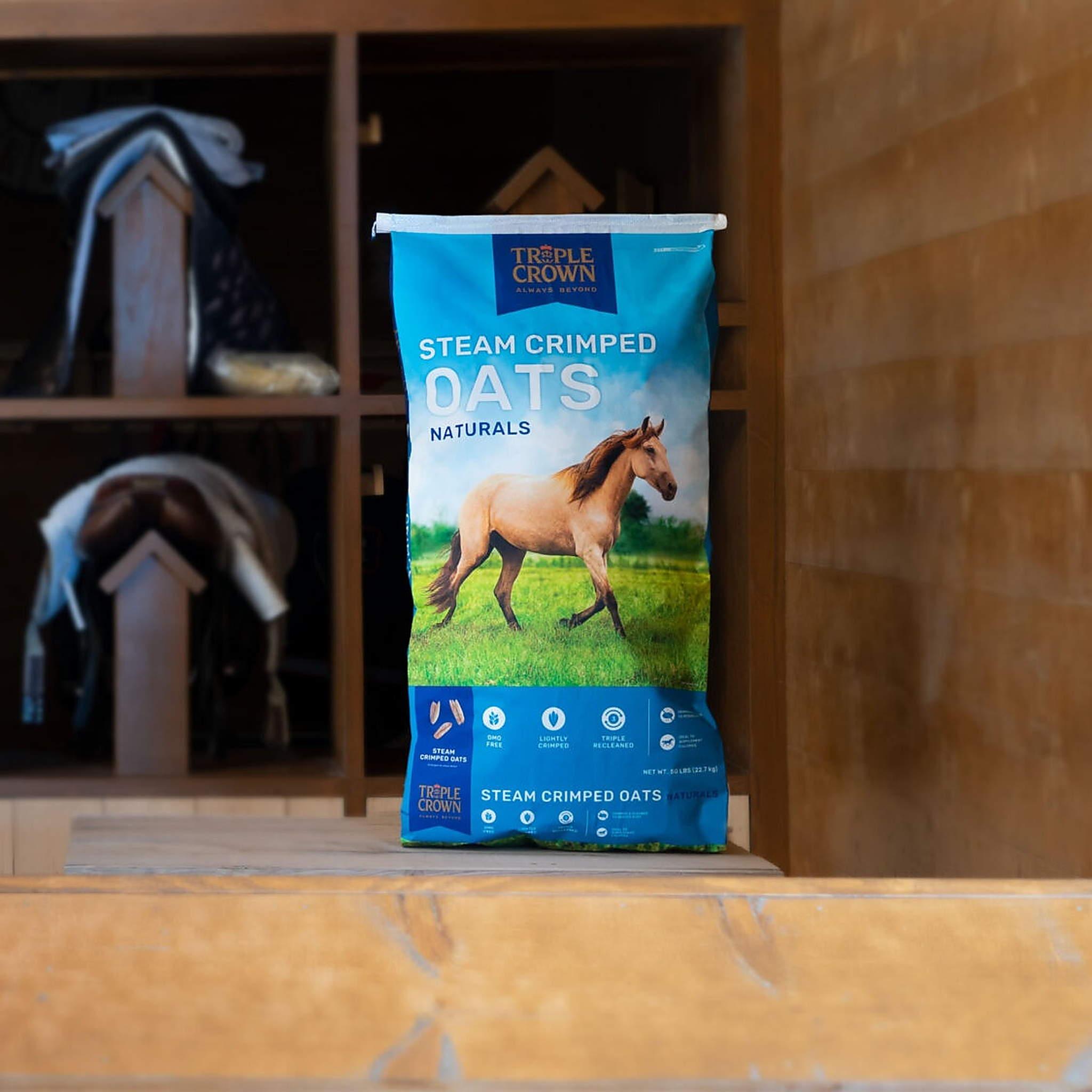 Triple Crown Naturals Steam Crimped Oats 50 lb bag on a bench in a barn tack room