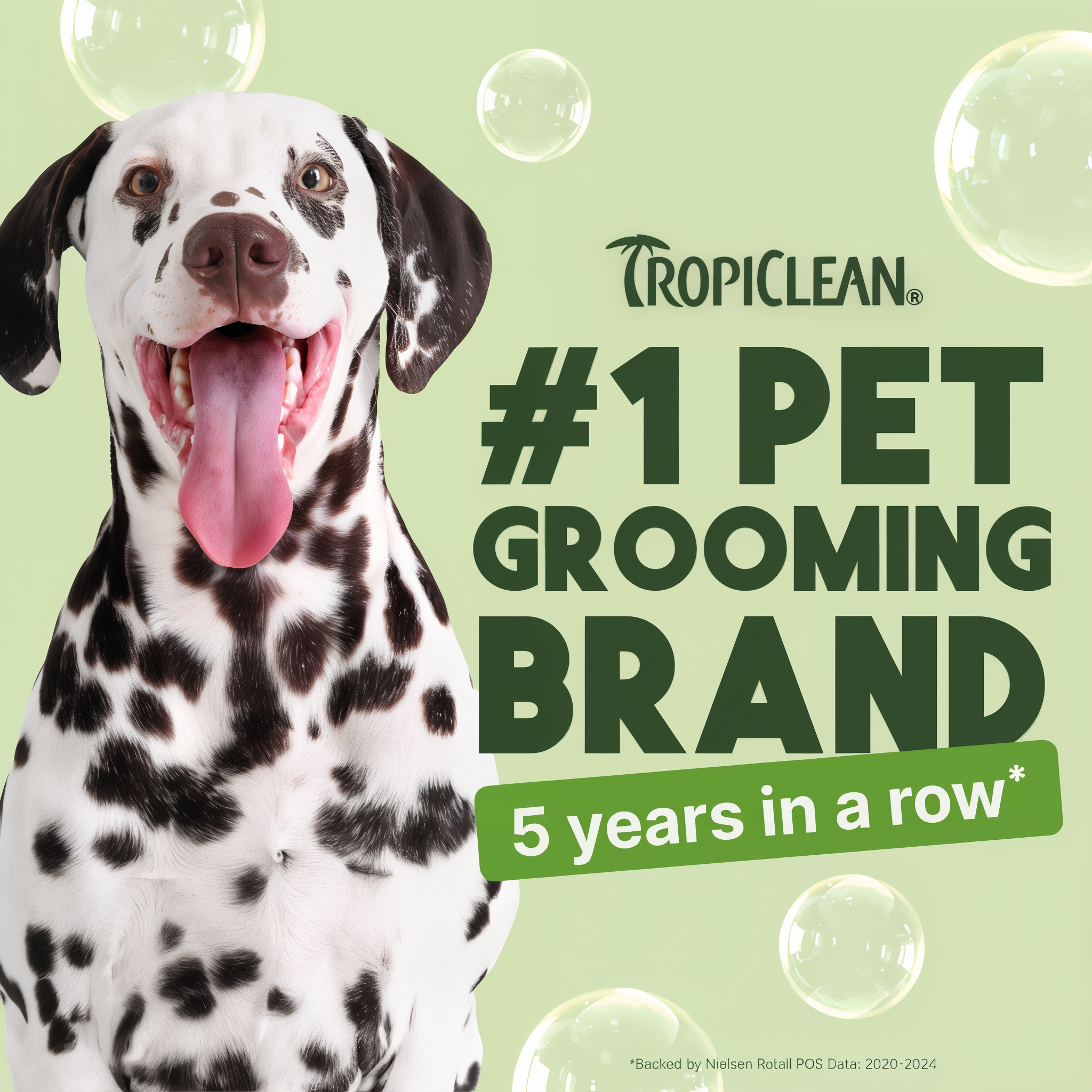 Black and white spotted dog with tongue out on pale green background with TropiClean branding and soap bubbles.